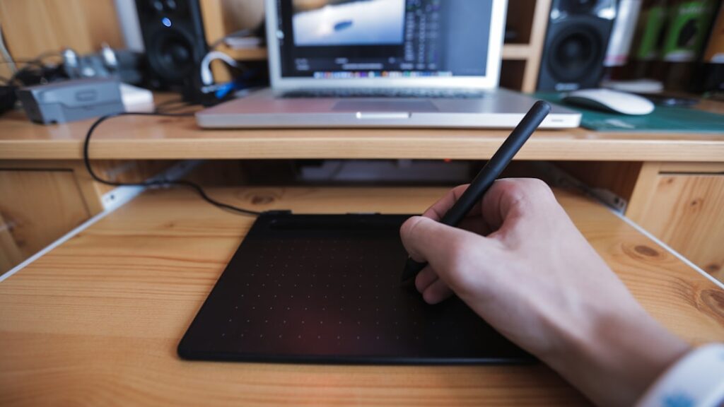 Hand using stylus on digital drawing tablet with computer setup, representing AI-powered image generation and digital art creation