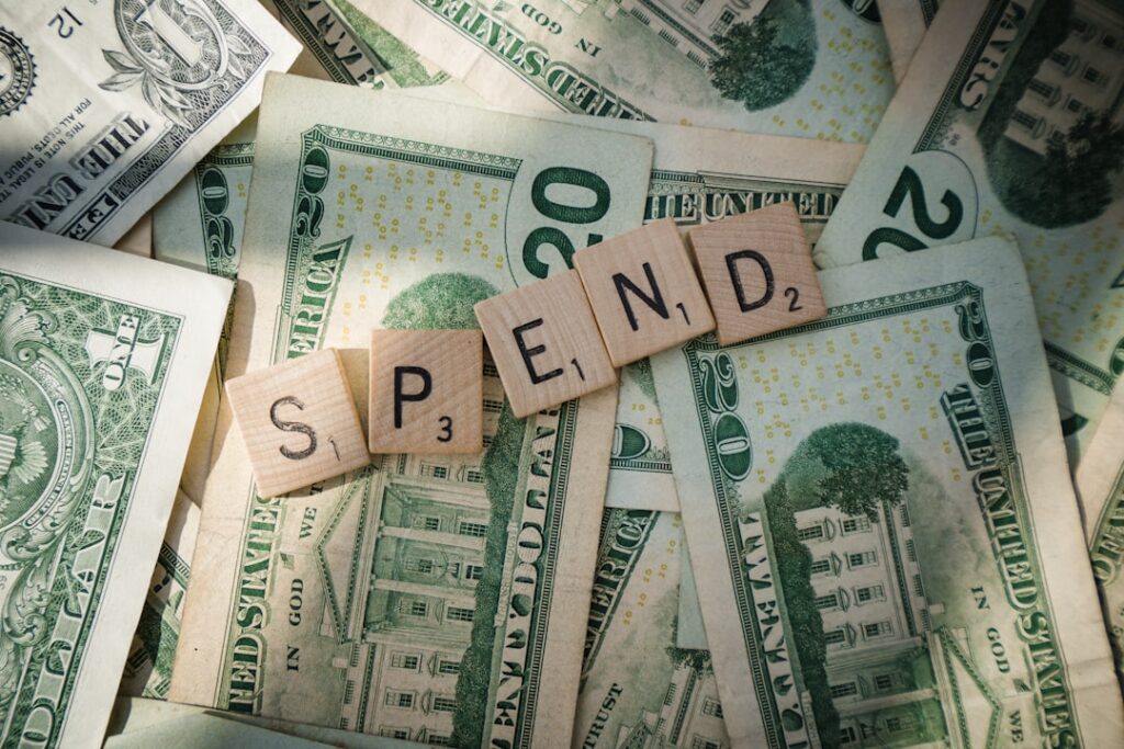 Scrabble letters spelling SPEND on dollar bills representing hidden costs in budget hosting