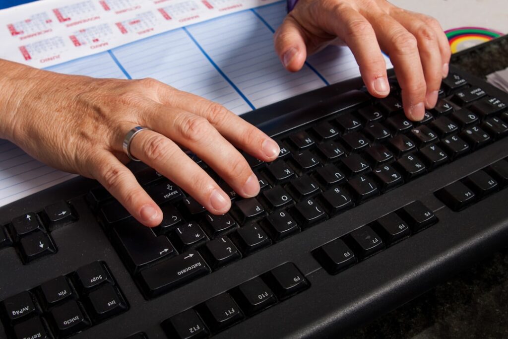 Hands typing on black keyboard at desk with papers, representing AI writing tools and content creation workflow