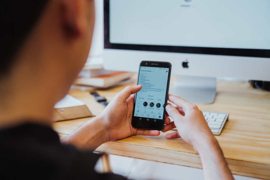 Person using smartphone while working at computer desk, representing the process of choosing and evaluating AI apps for productivity