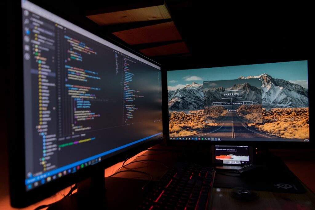 Dual monitor coding setup showing programming code for AI-assisted software development