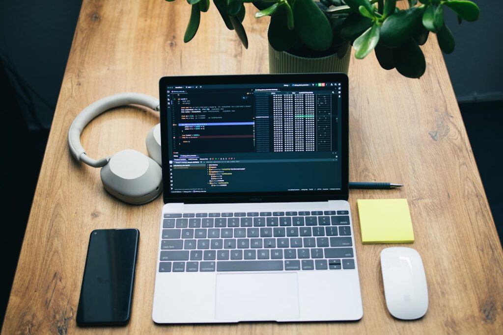 Laptop computer showing code on screen with headphones, phone, and workspace setup for AI software development