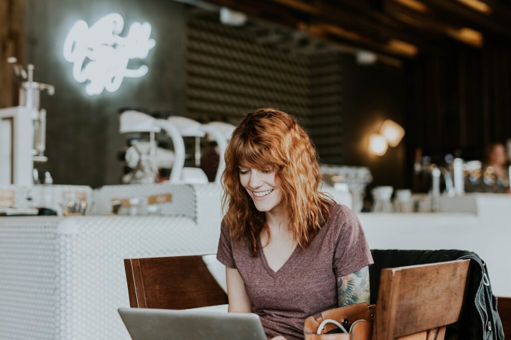 Solopreneur working on a laptop in a coffee shop, evaluating free AI chatbot tools for her small business workflow
