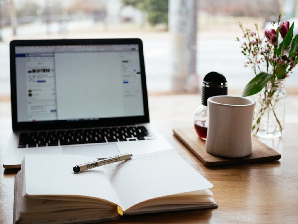 A blogger's workspace with an open notebook, pen, coffee mug, and laptop — representing the real-world content creation workflow that AI tools are meant to support