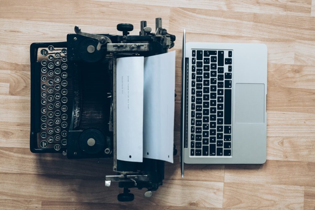 A vintage typewriter next to a modern MacBook laptop, symbolizing the evolution from traditional to AI-powered content creation tools