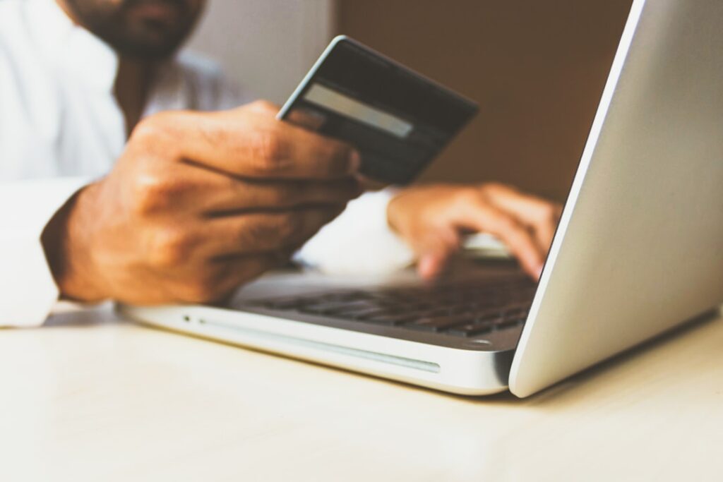 A person holding a credit card while using a laptop, representing the hidden subscription pricing gotchas when signing up for AI tools.