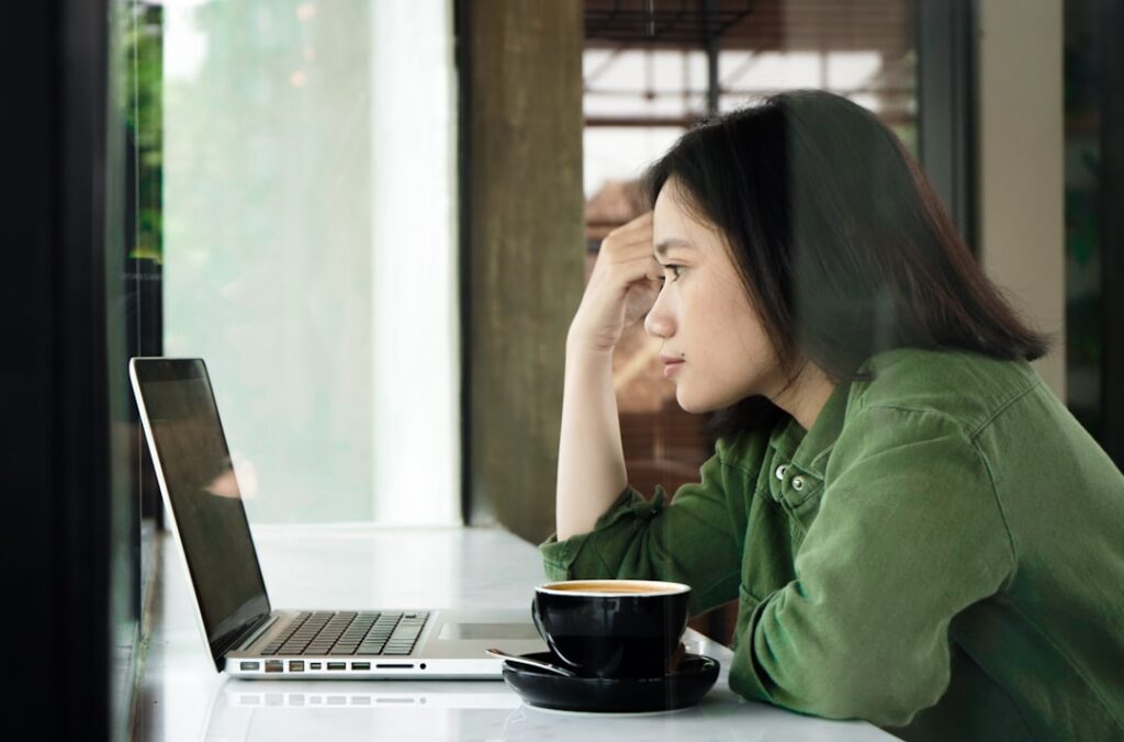 Woman looking overwhelmed while staring at a laptop screen with a coffee cup nearby, representing decision fatigue when choosing hosting