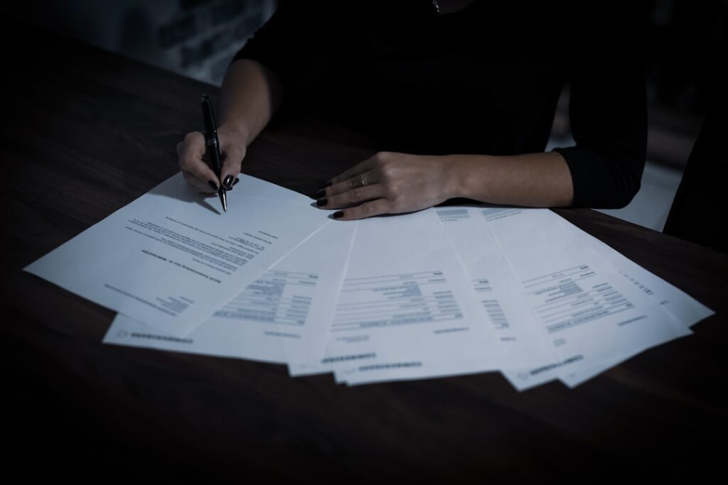 A person carefully reviewing multiple document pages spread on a dark table, representing the importance of scrutinizing AI tool subscription pricing and fine print before committing