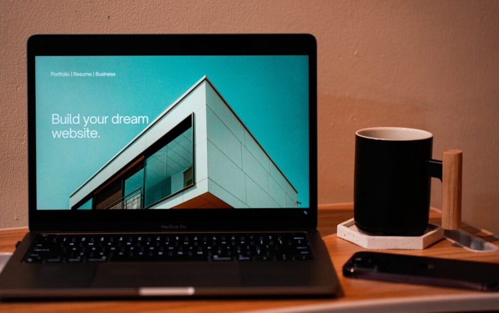 Laptop computer displaying website building interface with coffee mug on wooden desk. Photo by Mohammad Rahmani