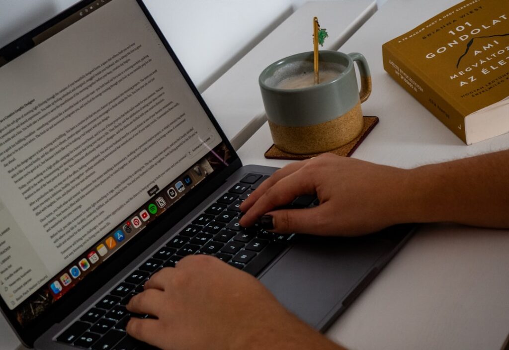 A content creator typing a blog post on a laptop with a coffee mug nearby, illustrating AI-assisted writing workflows