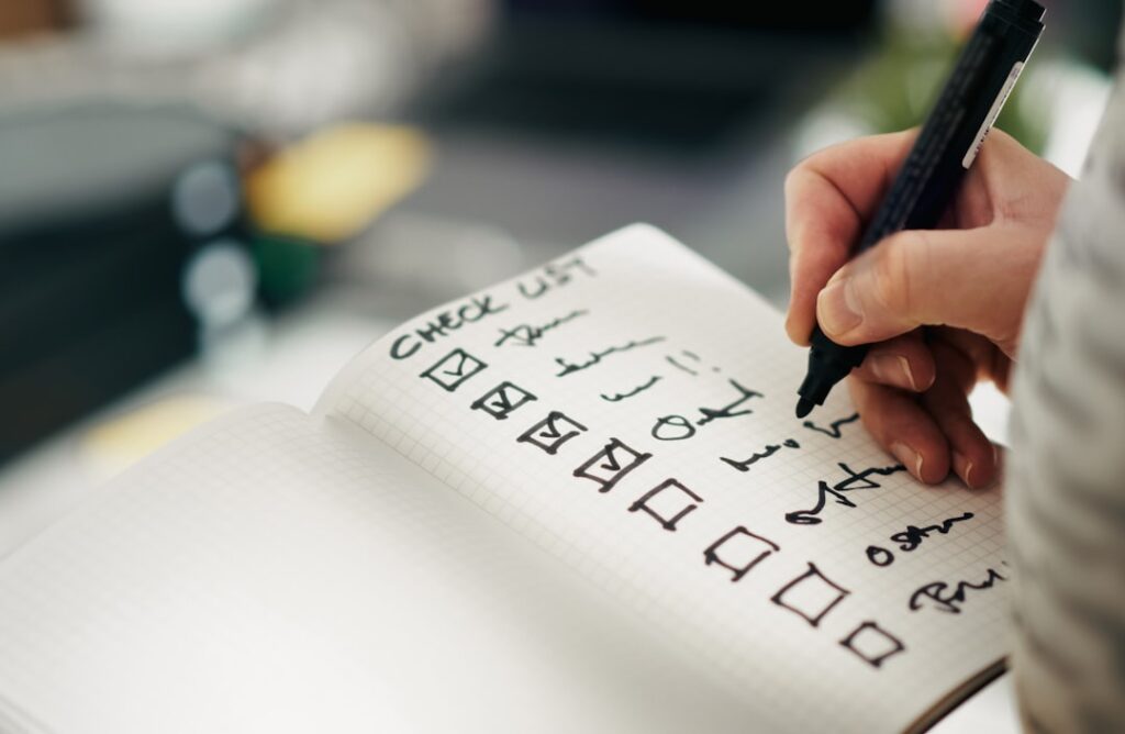 Hand writing a checklist in a notebook, representing the decision-making framework for evaluating whether WordPress is the right CMS choice