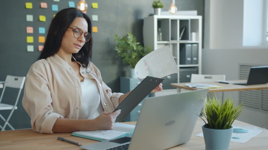 Professional analyzing documents while using laptop for AI-assisted writing and document processing