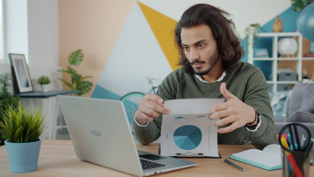 Small business owner analyzing hosting options and making decisions with laptop and documents