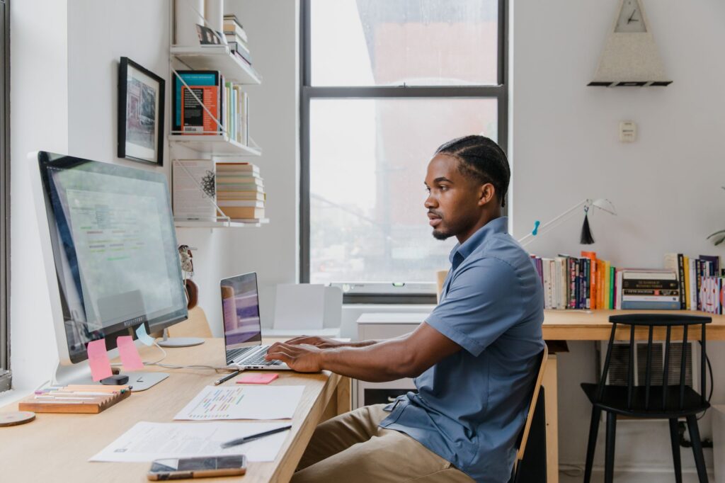A professional working on a laptop and desktop computer in a home office while setting up a WordPress site