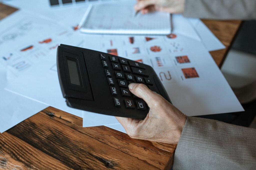 Hand holding a calculator on a wooden desk beside printed business charts and revenue graphs