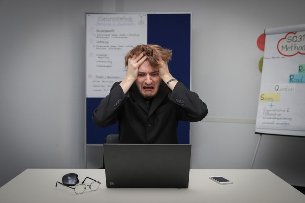 Frustrated person with hands on head sitting in front of a laptop, overwhelmed by complex software